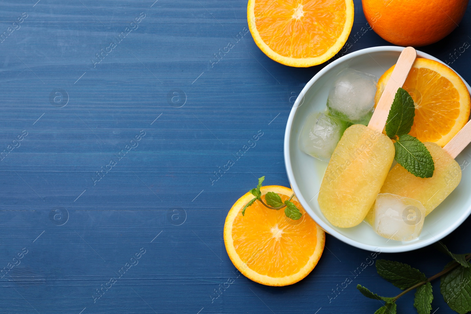Photo of Tasty orange ice pops and space for text on blue wooden table, flat lay. Fruit popsicle