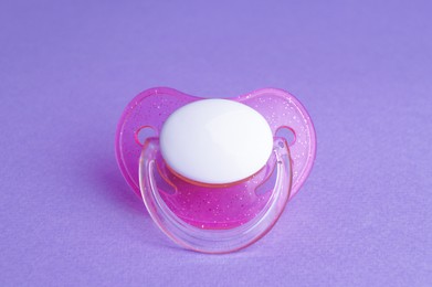 Photo of One new baby pacifier on purple background, closeup