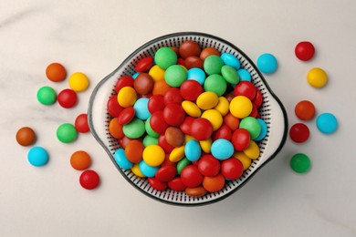 Photo of Bowl with tasty colorful candies on white table, flat lay