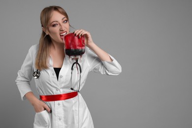 Photo of Woman in scary nurse costume with blood bag on light grey background, space for text. Halloween celebration