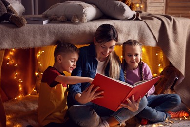 Photo of Mother and her children reading book in play tent at home