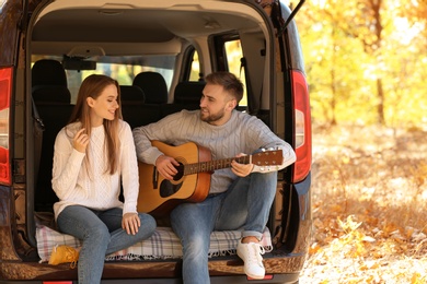 Photo of Young couple with guitar sitting in open car trunk outdoors
