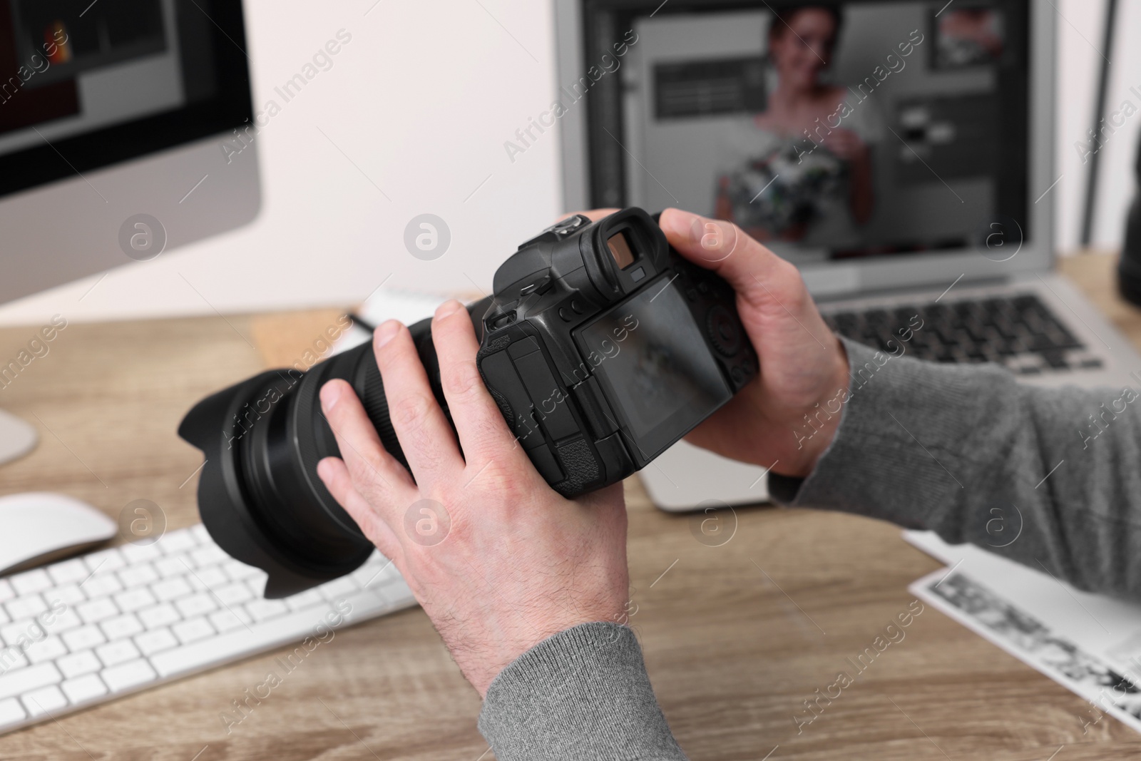 Photo of Professional photographer with digital camera at wooden table indoors, closeup