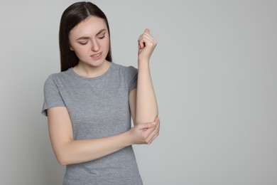 Photo of Young woman suffering from pain in her elbow on light grey background, space for text. Arthritis symptoms