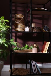 Photo of Stylish wicker candle holder, night lamp with incandescent bulb and decor on shelving unit near brown wall