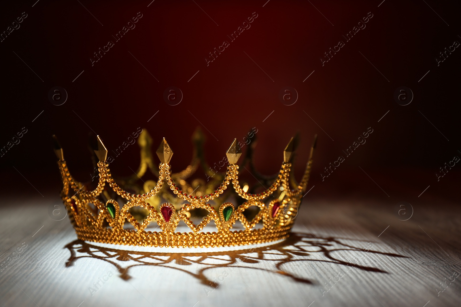 Photo of Beautiful golden crown with gems on wooden table. Fantasy item