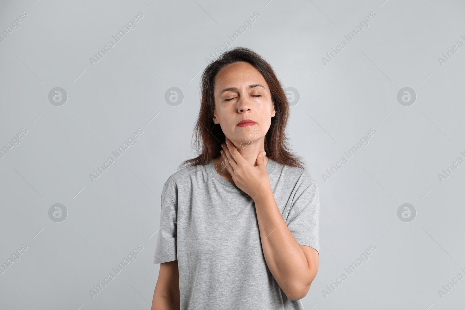 Photo of Mature woman doing thyroid self examination on light background