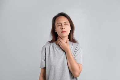 Photo of Mature woman doing thyroid self examination on light background