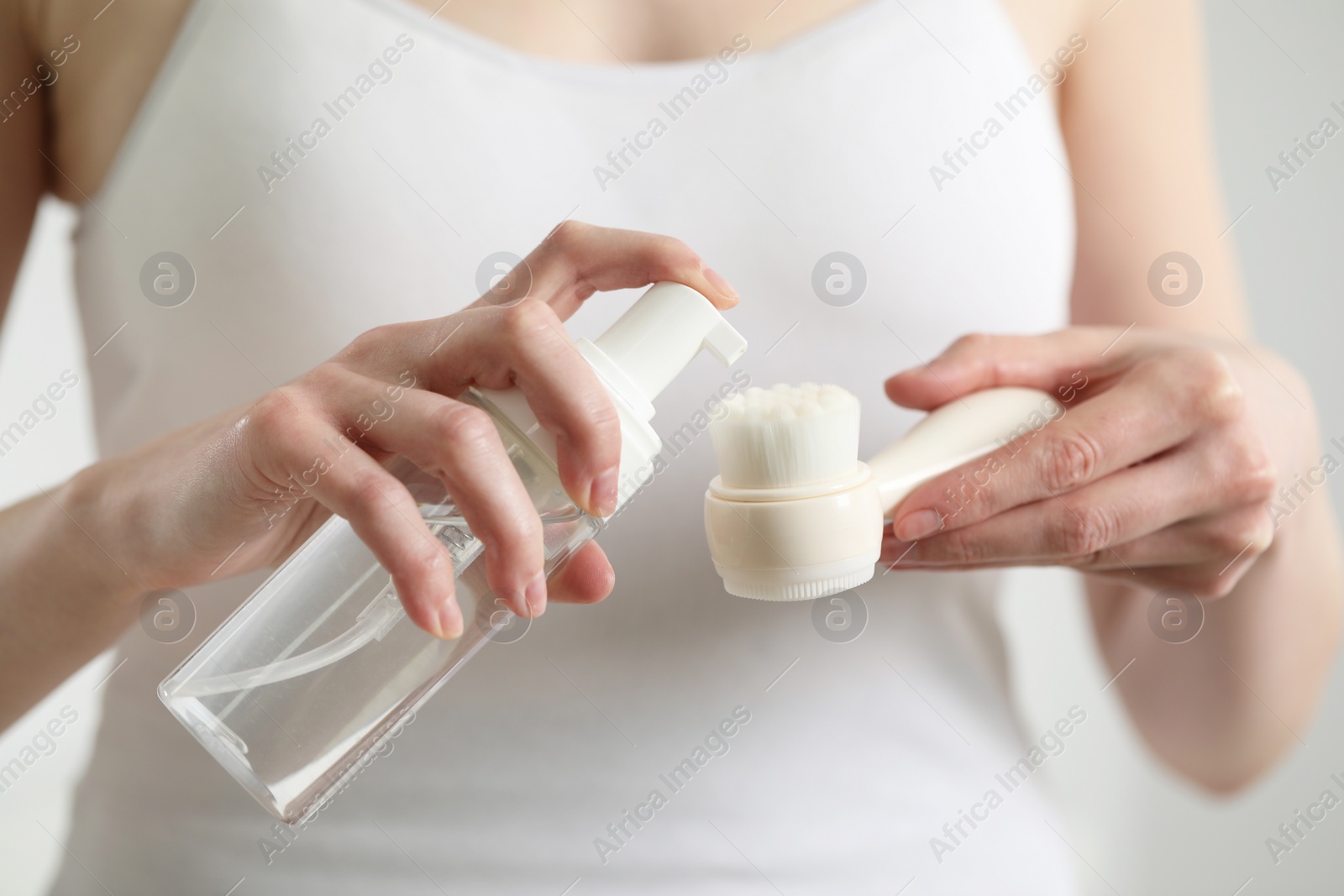 Photo of Washing face. Woman applying cleansing foam onto brush against light background, closeup