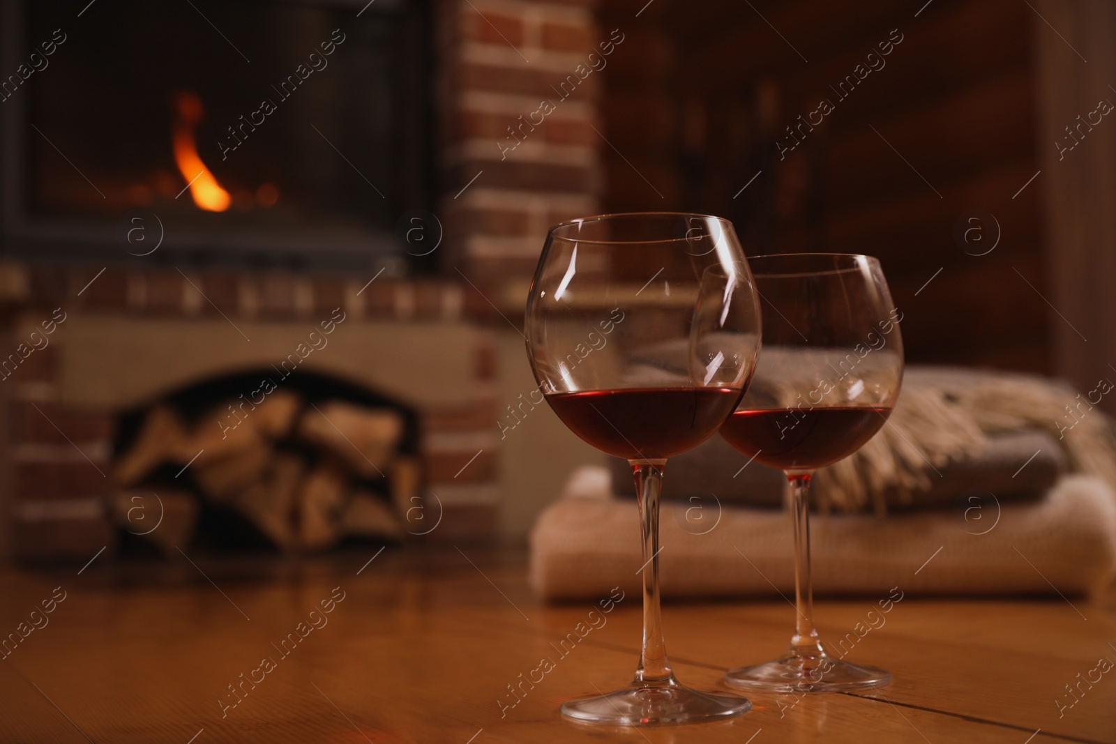 Photo of Glasses of red wine on wooden floor near fireplace. Space for text