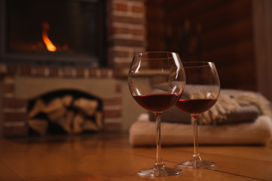 Glasses of red wine on wooden floor near fireplace. Space for text