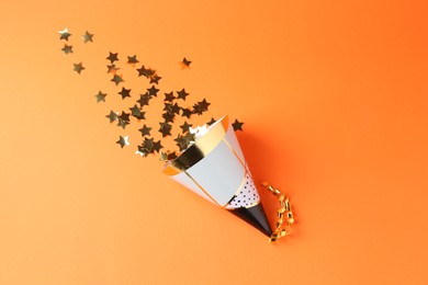 Party hat and confetti on orange background, top view