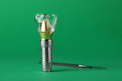 Educational model of dental implant near medical tool on green background. Space for text