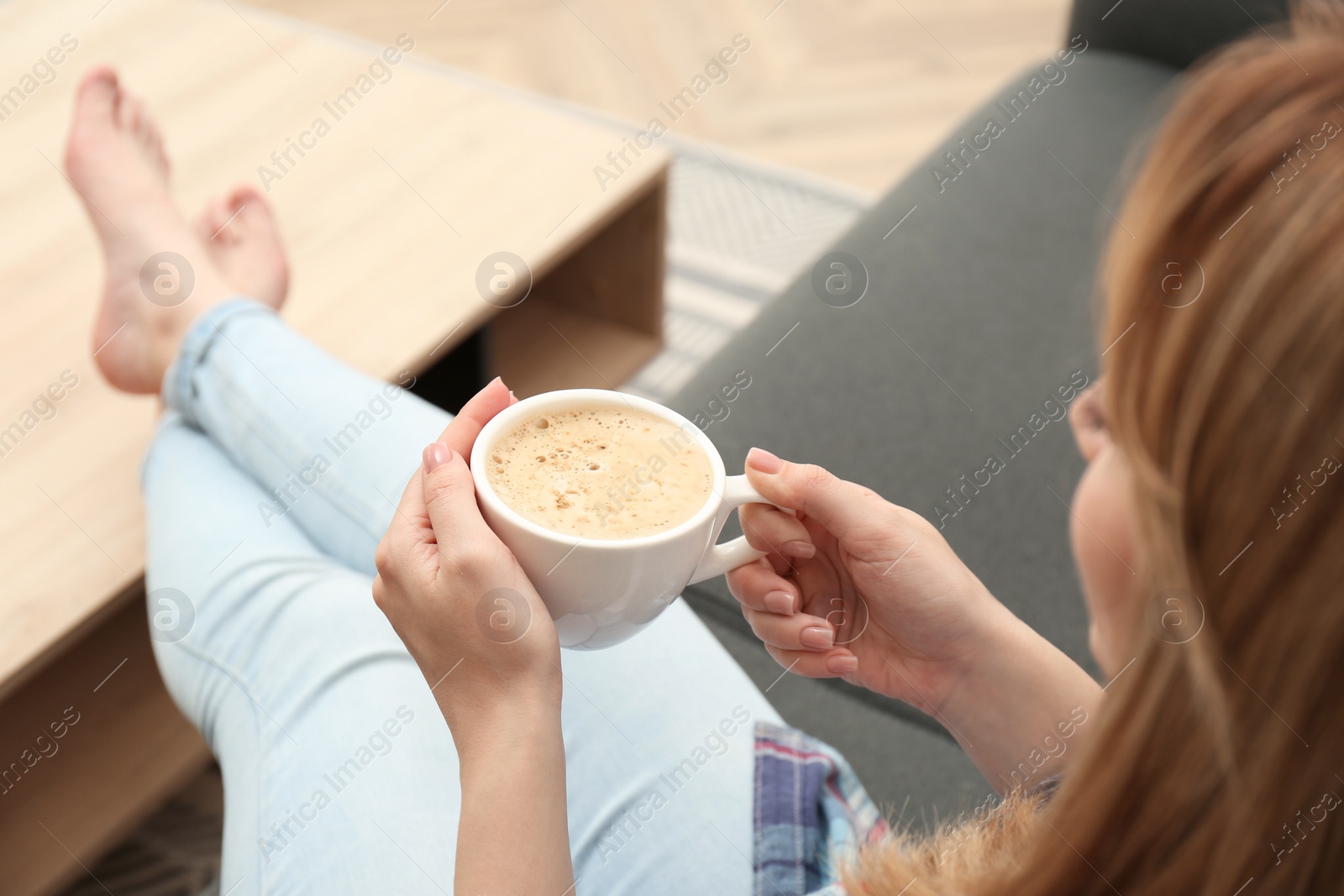 Photo of Young woman with cup of coffee relaxing on sofa at home, closeup