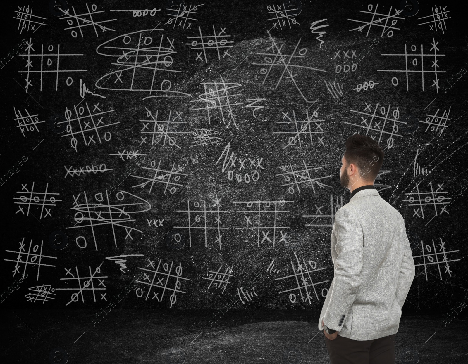 Image of Young businessman in elegant suit near blackboard with drawn tic tac toe game 