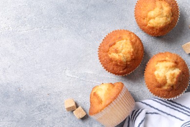 Photo of Delicious sweet muffins and brown sugar on light grey textured table, flat lay. Space for text