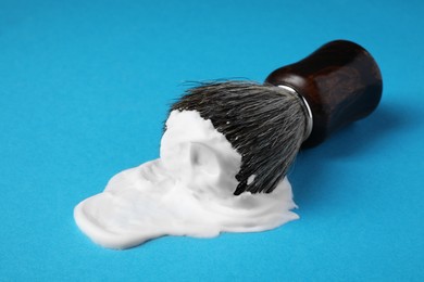 Photo of Brush with shaving foam on blue background, closeup