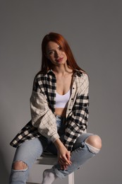 Beautiful young woman sitting on white stool against gray background