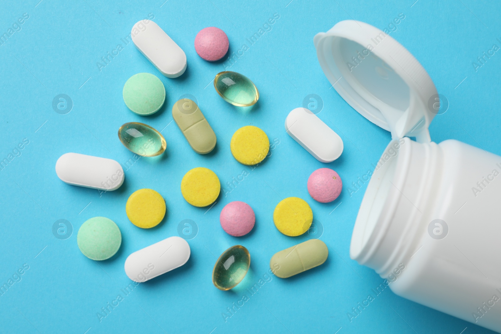 Photo of White bottle and different vitamin pills on light blue background, top view