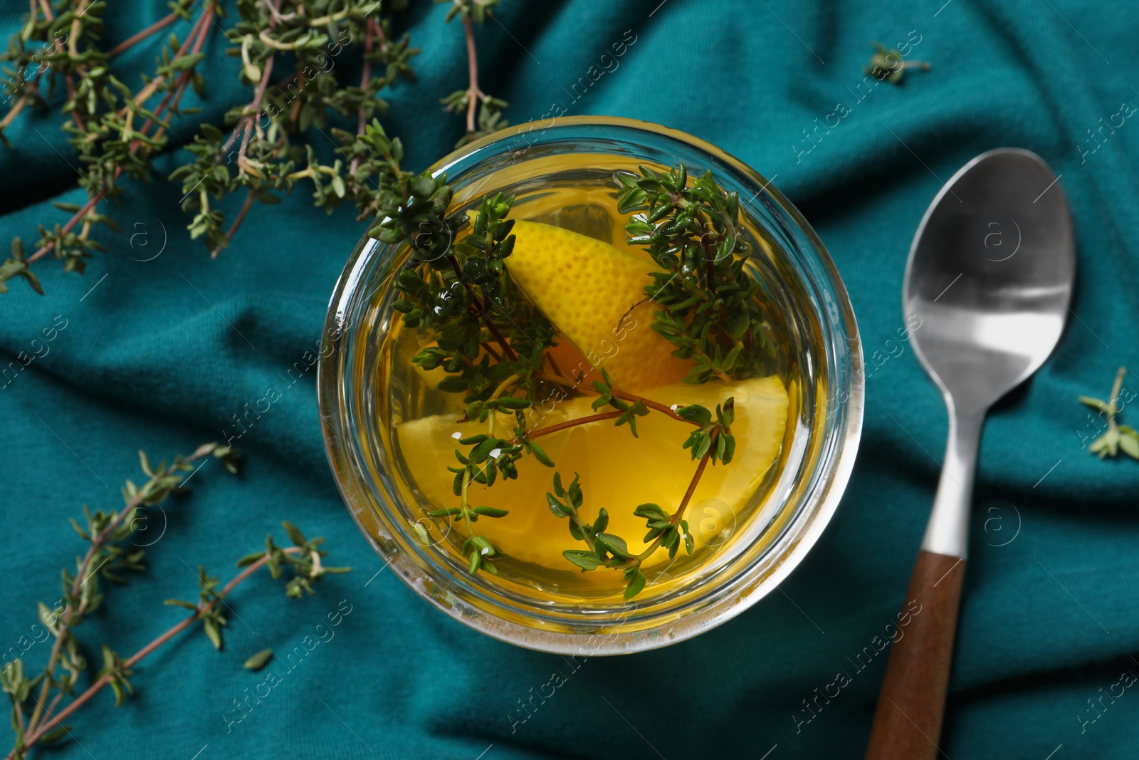 Photo of Glass of aromatic herbal tea with thyme and lemon on teal fabric, flat lay