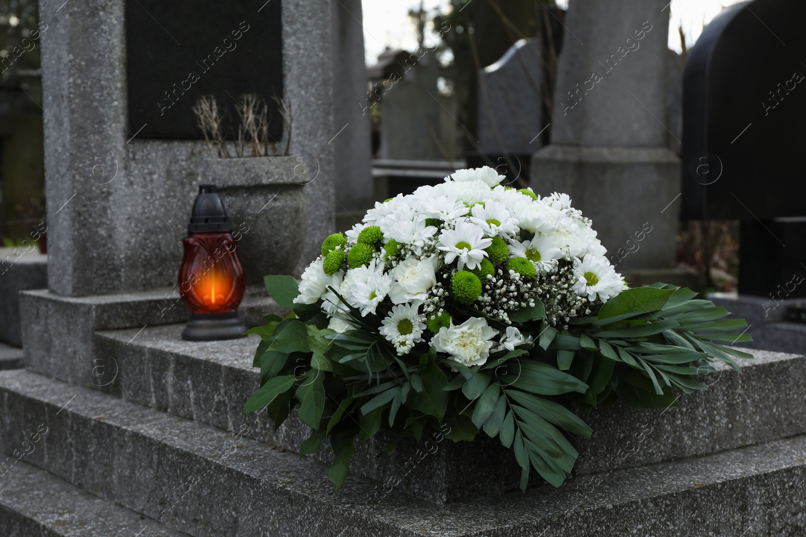 Photo of Funeral wreath of flowers and grave lantern on granite tombstone in cemetery