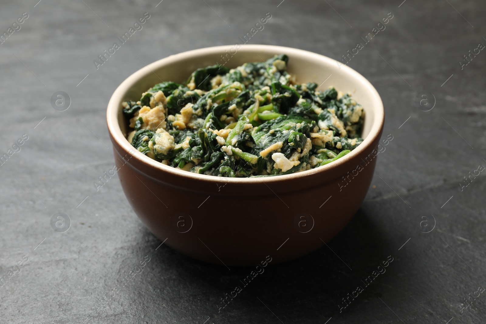 Photo of Tasty spinach dip with egg in bowl on black table, closeup