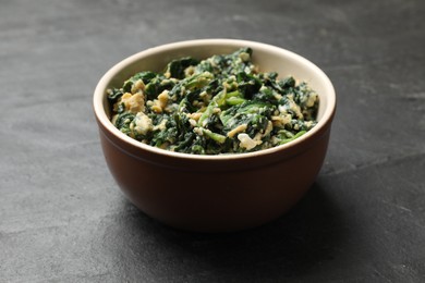 Photo of Tasty spinach dip with egg in bowl on black table, closeup