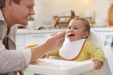 Photo of Father feeding his cute little baby in kitchen