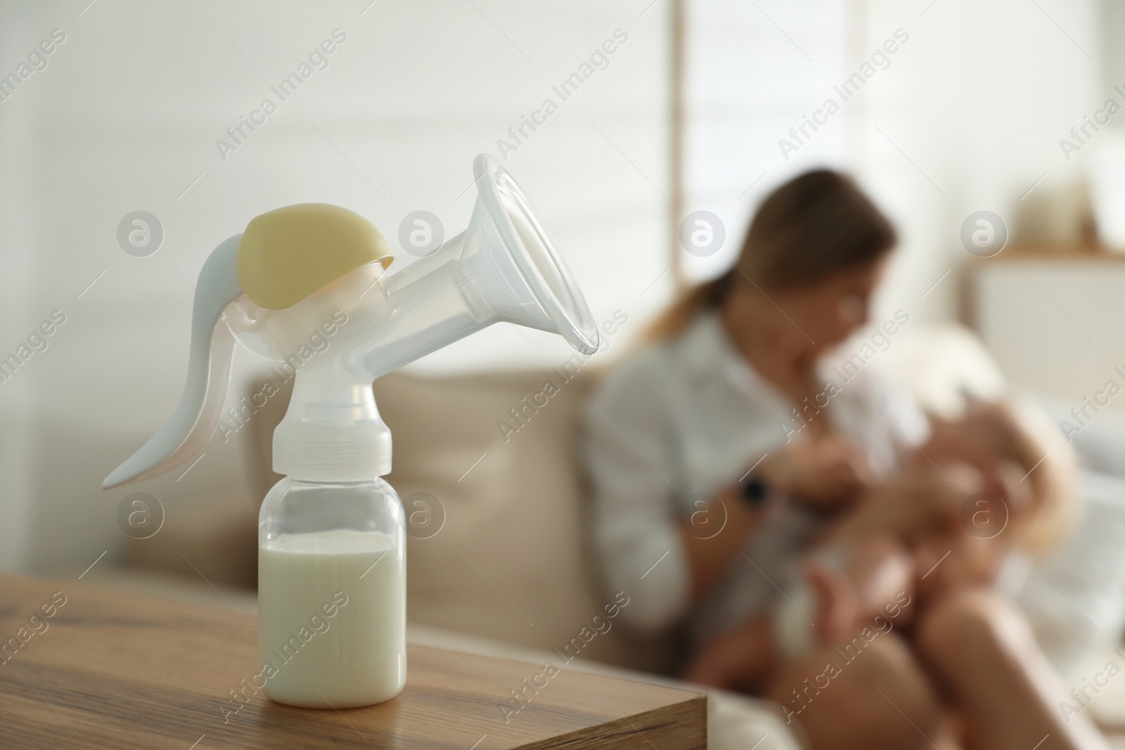 Photo of Mother feeding her little baby at home, focus on breast pump with milk. Healthy growth