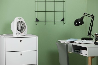 Photo of Modern electric fan heater on chest of drawers in room