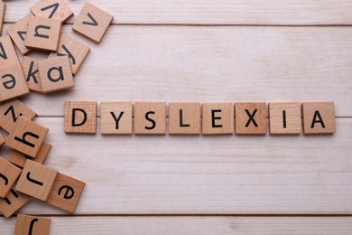 Photo of Tiles with word Dyslexia on wooden table, flat lay