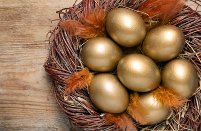 Photo of Many golden eggs in nest on wooden table, top view