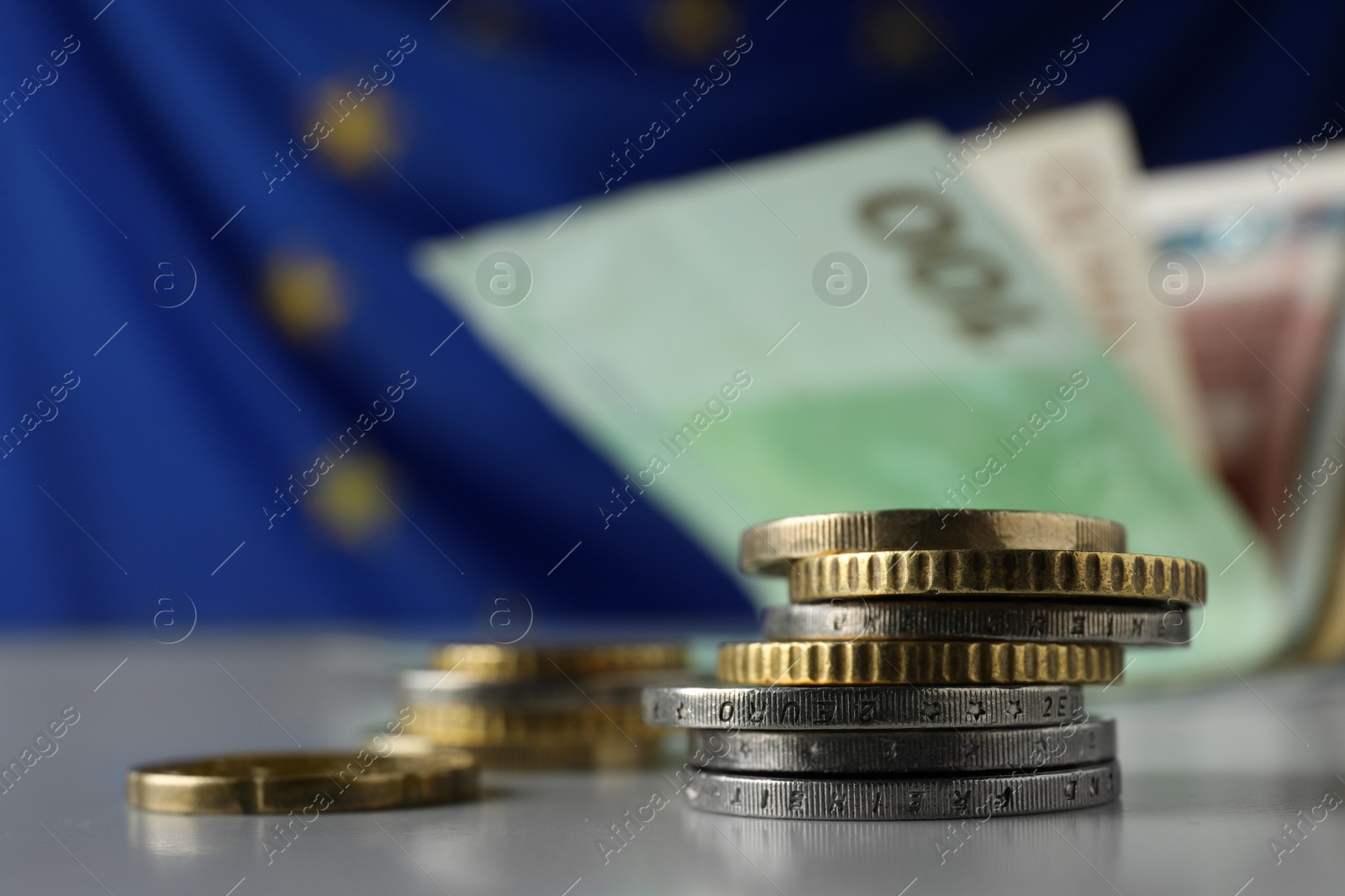 Photo of Many different coins on table against banknotes and European Union flag, closeup. Space for text