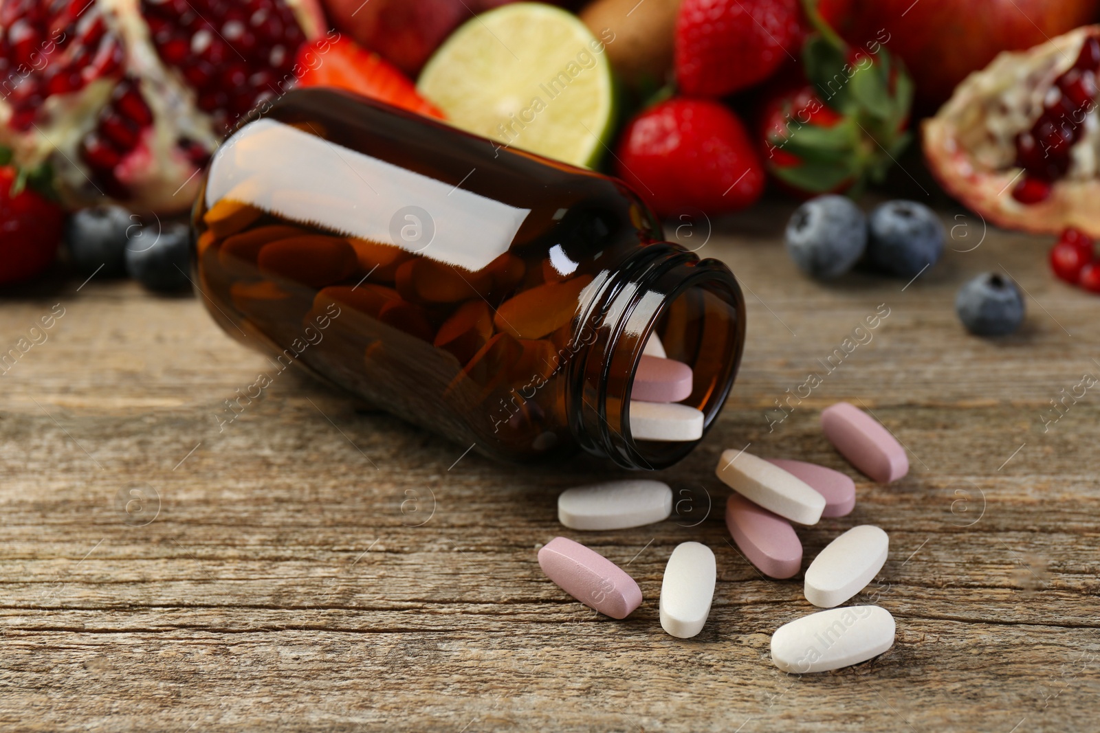 Photo of Vitamin pills, bottle and fresh fruits on wooden table, closeup