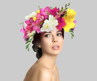 Pretty woman wearing beautiful wreath made of flowers on light grey background