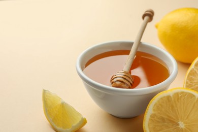 Photo of Ripe lemons, bowl of honey and dipper on beige background, closeup. Space for text