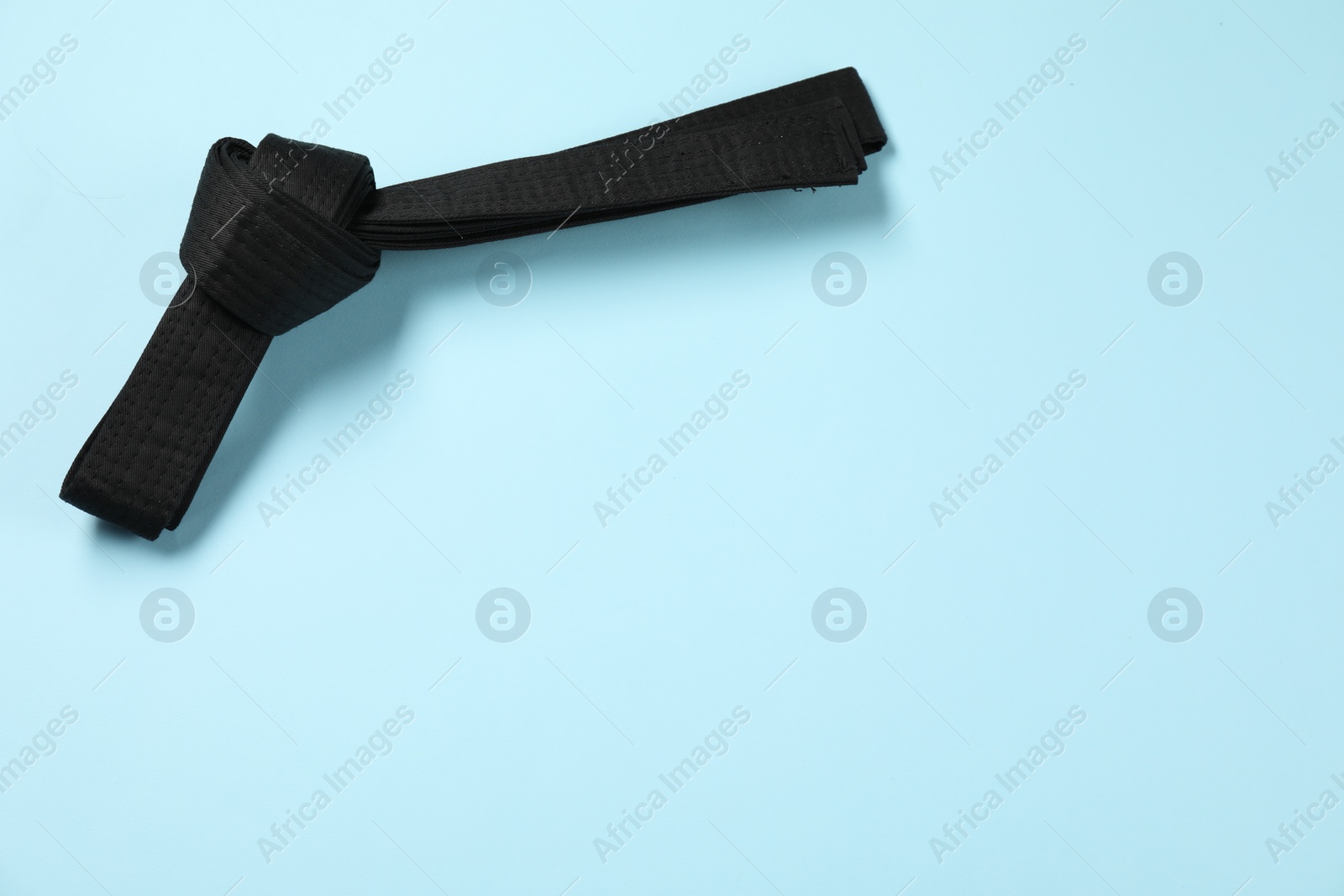 Photo of Black karate belt on light blue background, top view. Space for text