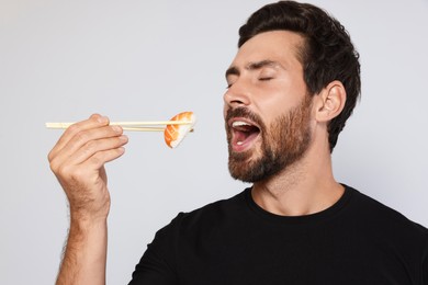 Photo of Handsome man eating tasty sushi with chopsticks on light grey background