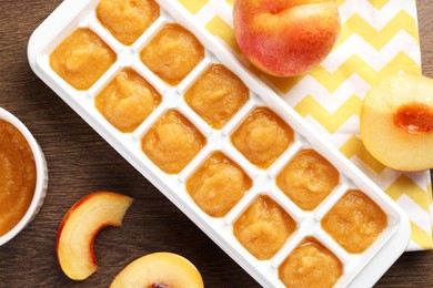 Nectarine puree in ice cube tray and fresh nectarine fruits on wooden table, flat lay. Ready for freezing