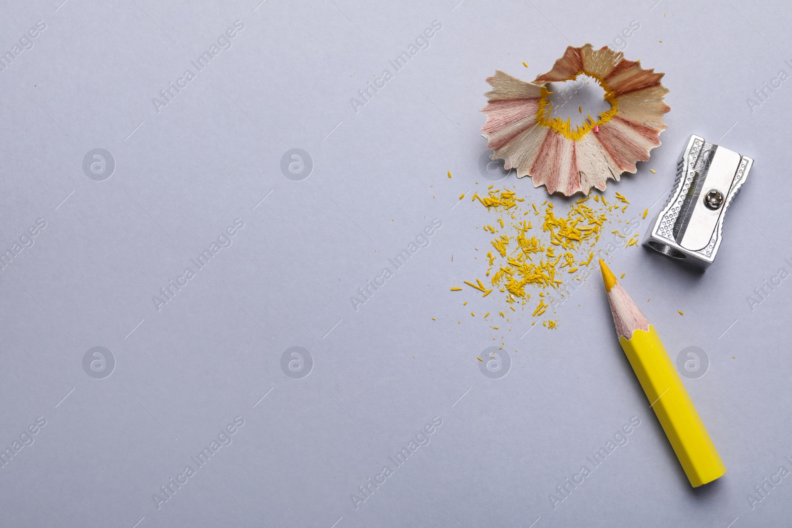 Photo of Yellow pencil, shaving, crumbs and sharpener on grey background, flat lay. Space for text