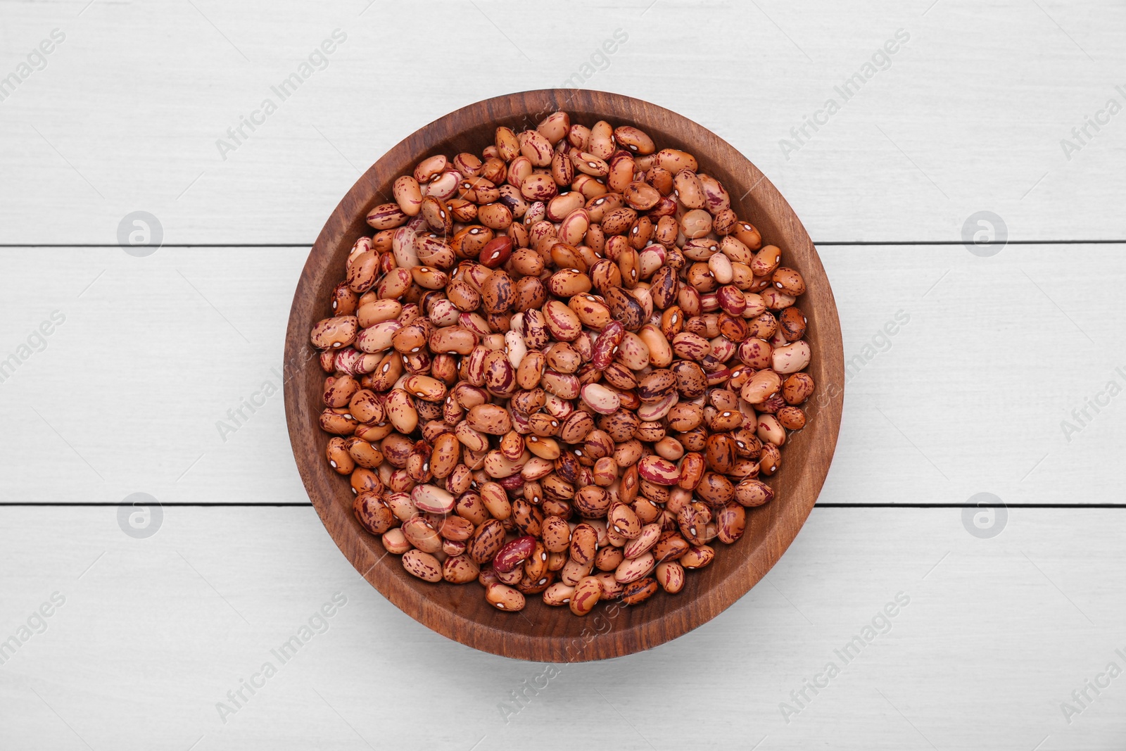 Photo of Bowl with dry kidney beans on white wooden table, top view