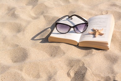 Photo of Beautiful sunglasses, book and starfish on sand, space for text