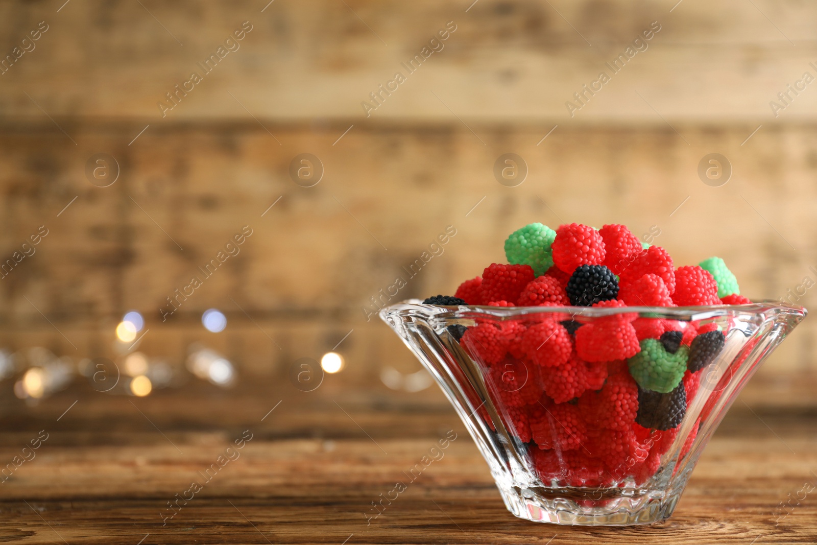 Photo of Delicious jelly candies in bowl on wooden table, closeup. Space for text