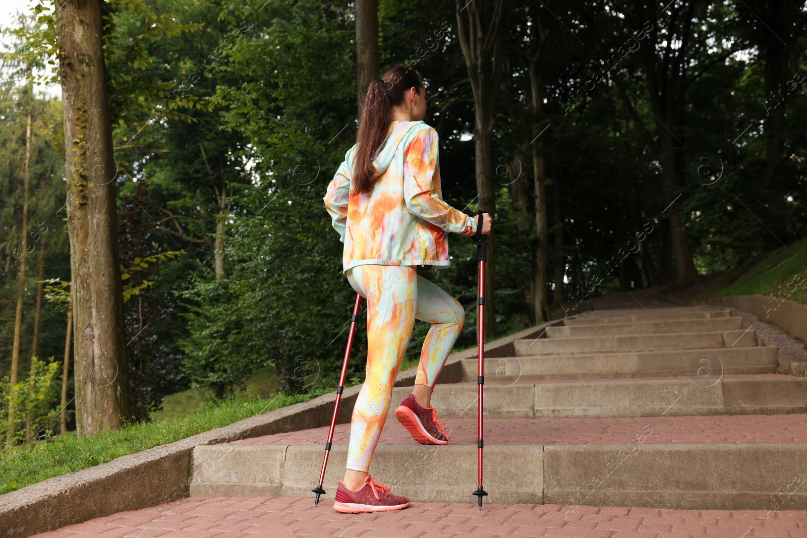 Photo of Young woman practicing Nordic walking with poles on steps outdoors, low angle view