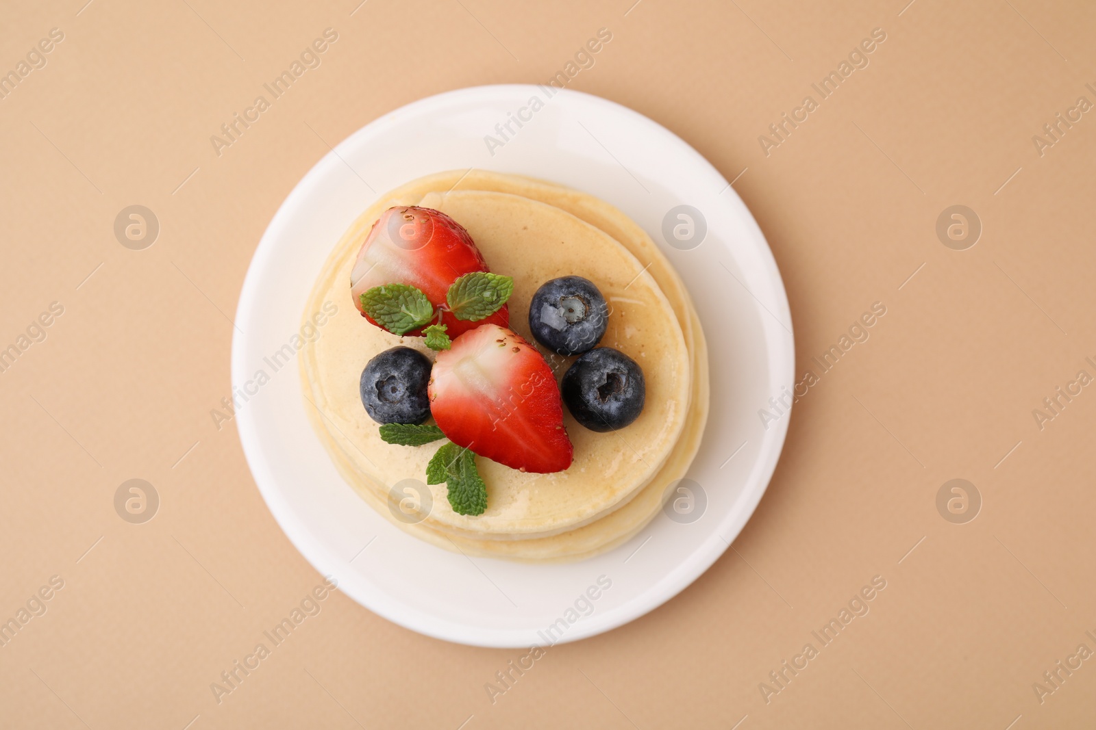 Photo of Stack of tasty pancakes with fresh berries and mint on beige background, top view