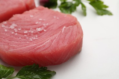 Raw tuna fillets with salt and parsley on white table, closeup. Space for text