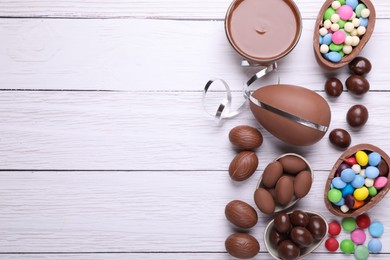 Delicious chocolate eggs, paste and candies on white wooden table, flat lay. Space for text