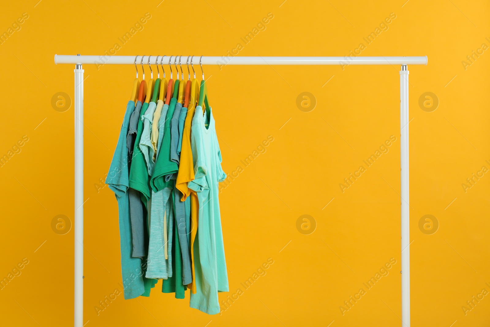 Photo of Rack with stylish children clothes on yellow background