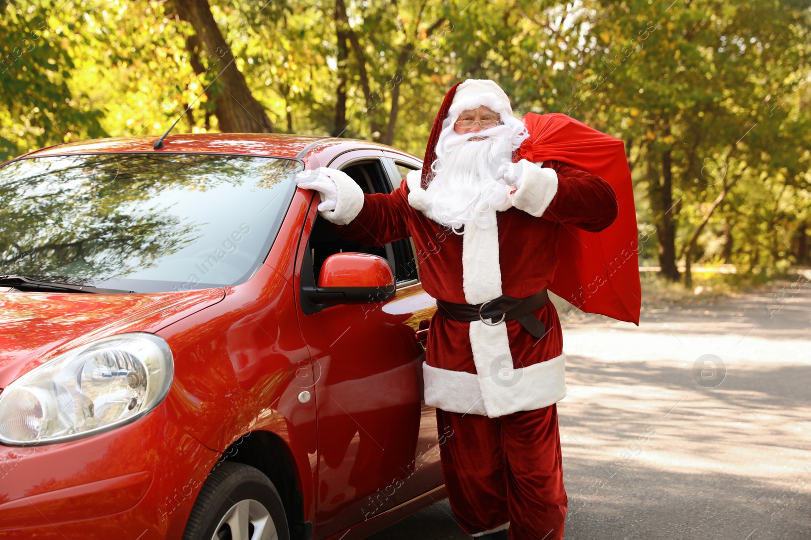 Photo of Authentic Santa Claus with bag full of presents near car outdoors