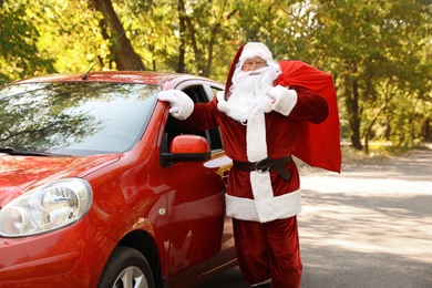 Photo of Authentic Santa Claus with bag full of presents near car outdoors